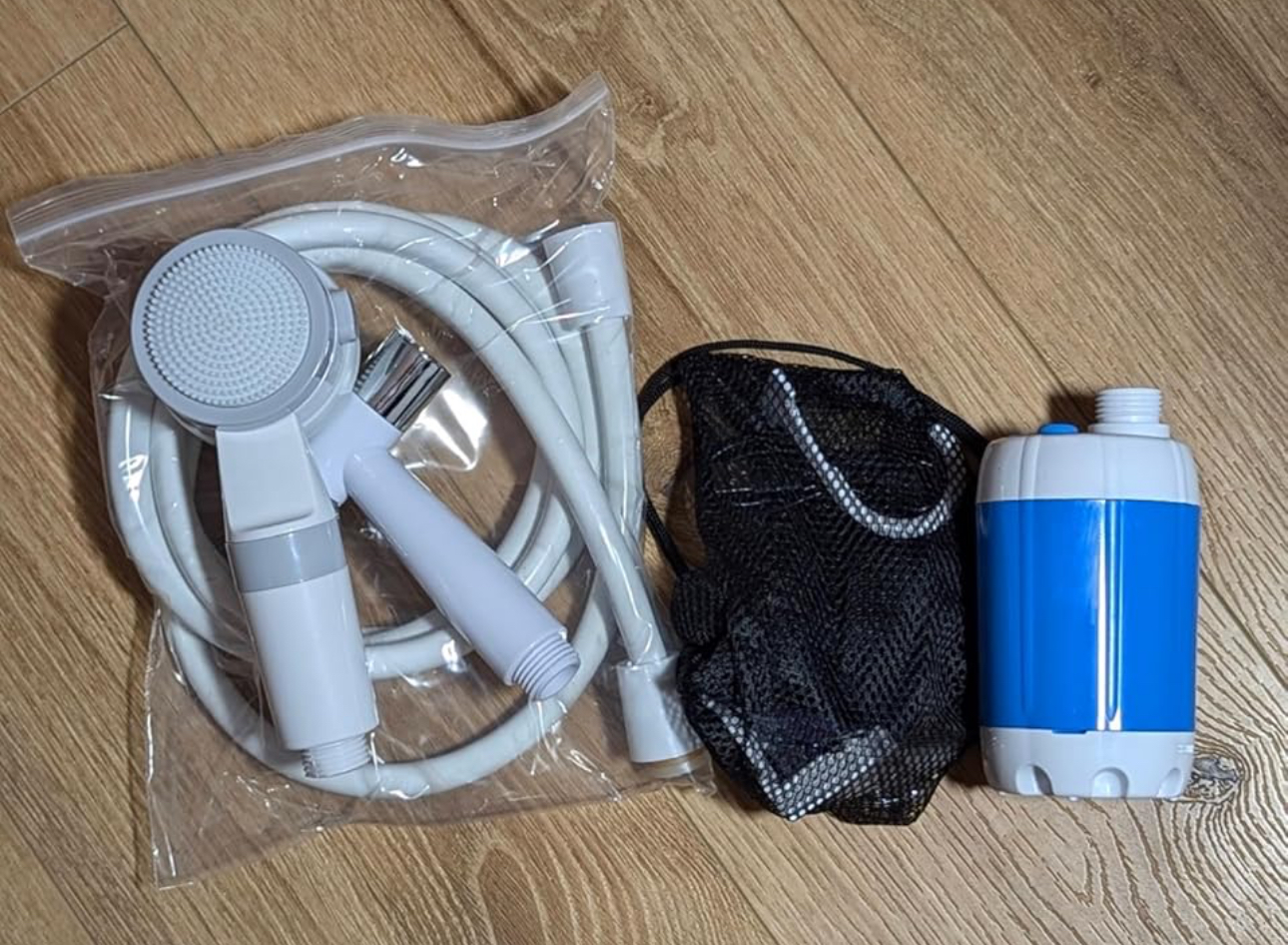 Portable shower parts and bag laid out on a wood floor